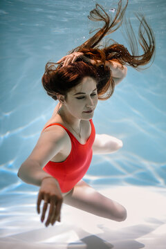 A girl swims under the water in a red bodysuit