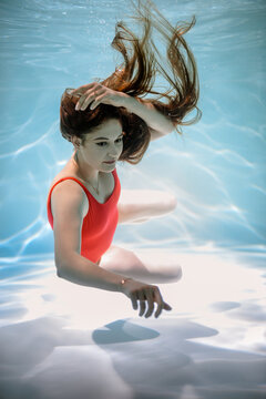 A girl swims under the water in a red bodysuit