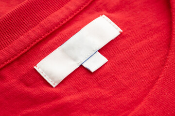 White blank clothing tag label on new red cotton shirt fabric texture background