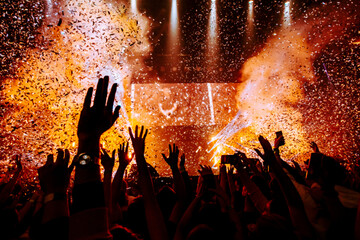 Fans hands raised up during the show. Bright lights and shiny confetti at a pop concert. happy youth dancing at a festival in a crowd. view of the stage.