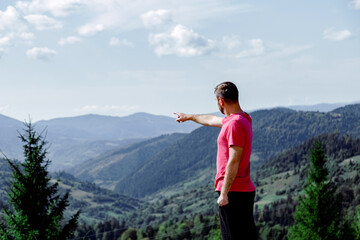 Naklejka premium Man points his hand towards mountains. unrecognizable man from the back stands in front of mountain landscape and blue sky