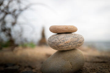 Three zen-like rocks on the blurred tree, sky, and sea background, selective focus image for mindfulness and tranquility themes.
