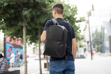 Rear view man walking in city with black leather backpack on his shoulders
