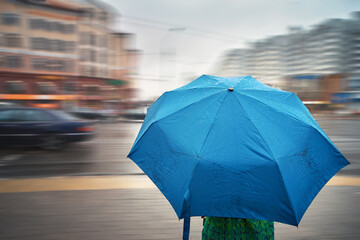Woman with wet umbrella walking in rainy day on city street. Woman under umbrella, waiting to cross the road on pedestrian crossing. Surface of blue umbrella with rain drops