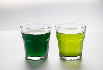 Dissolved powder spirulina and chlorella in a transparent glass cups on a white background.