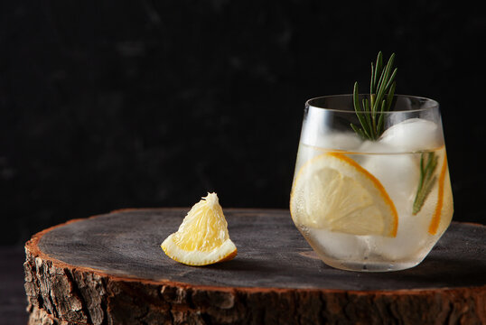refreshing drink with lemon rosemary and ice on dark wooden background