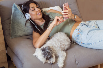 Beautiful Young Woman with Headphones Listening Music at Home with her Dog