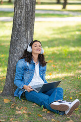 Vertical photo of a 40-years-old woman with laptop in city park during online vido call. Online working concept.