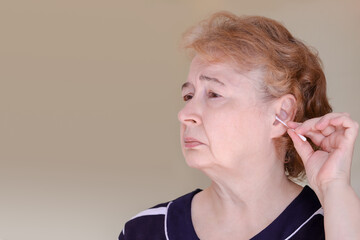 an elderly Caucasian woman cleans her ear with a cotton swab