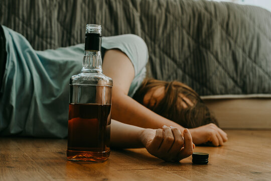 Woman lying on the floor with an alcohol bottle and sleeping, overdosage and female alcoholism concept.
