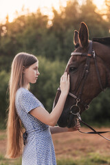 Obraz premium A young beautiful girl with long hair strokes a horse and looks at her in the summer in nature.