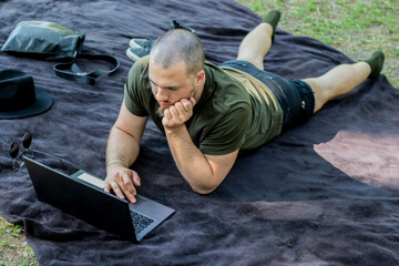 shaved head caucasian male reading his computer in a park.