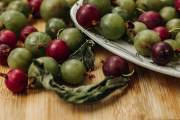 Green and red gooseberries. Gooseberries on a wooden surface and on a white plate. A plate with gooseberries. Dry mint leaf