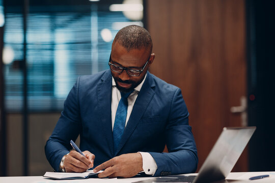 Portrait smiling african american businessman signs contract sit at table for meeting in office with notebook with pen and laptop