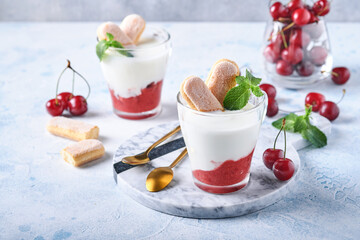 Summer cherry puff pastry with savoiardi cookies and cream cheese in glass on light grey background. Traditional tiramisu cake with fresh berries. Selective focus.