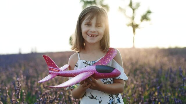 Portrait happy kid with toy airplane against summer sky background. Girl with airplane on a summer lavender field. Best childhood and big child dream concept