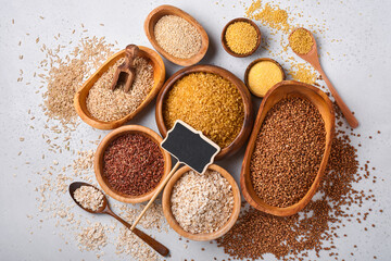 White, brown and red rice, buckwheat, millet, corn groats, quinoa and bulgur in wooden bowls on the light gray kitchen table. Gluten-free cereals. Top view with copyspace