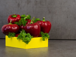 Red, bell peppers and parsley close-up lie in a wooden box. Gray background. Vegetables.