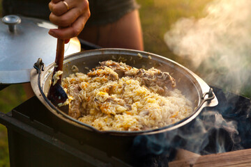 The female hand of the cook is stirring the pilaf with a spoon.