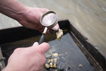 Treasure hunter is picking a golden ore from dirty metal grid on the river water background....