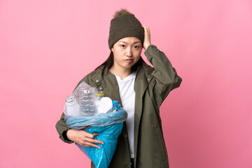 Chinese girl holding a bag full of plastic bottles to recycle over isolated pink background with an...