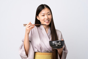 Young Chinese girl wearing kimono over isolated white background holding a bowl of noodles with chopsticks