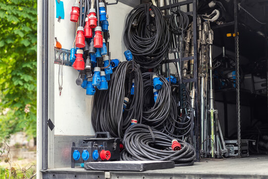 Open cargo box of filming movie set production equipment transport truck van vehicle with many electrical cables wire, rack and sockets on city streey outdoors. Cinema or television supply rental car