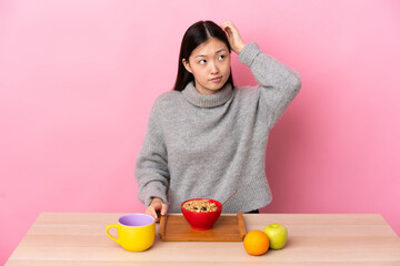 Young Chinese girl  having breakfast in a table having doubts while scratching head