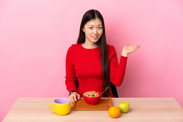 Young Chinese girl  having breakfast in a table holding copyspace imaginary on the palm to insert...
