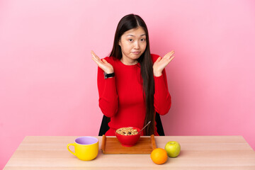 Young Chinese girl  having breakfast in a table making doubts gesture