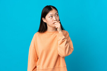 Young Chinese girl over isolated blue background having doubts and with confuse face expression