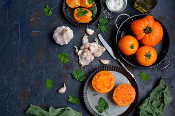 Yellow juicy tomatoes, garlic, parsley, olive oil on a dark blue background. View from above. Cooking in the kitchen