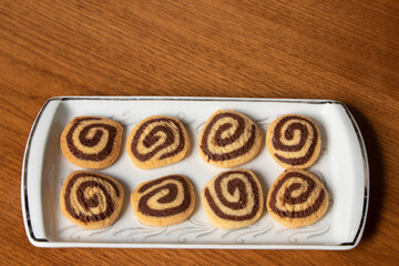 delicious buttery cookies decorated with chocolate spiral, served for breakfast on white rectangular plate on wooden table