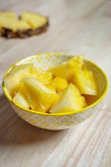 nice yellow bowl filled with pieces of delicious yellow pineapple on light wooden table