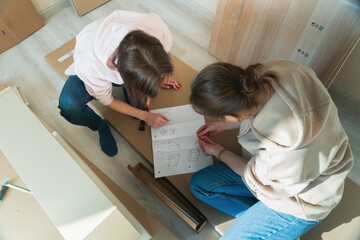Women reading instructions to assemble furniture. Moving in new house