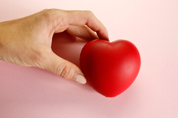 hand holding red heart on pink background