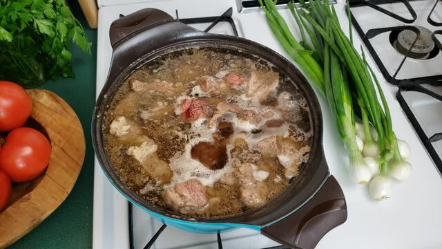 Home cooking - Top view of boiling lot of meat in non stick pot on gas stove while lot of scum float on surface of broth or stock ready to be collected.