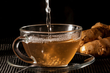 Xicara de chá de gengibre sobre superfície com raízes de gengibre ao fundo. 