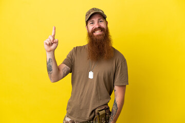 Redhead Military man with dog tag isolated on yellow background showing and lifting a finger in...