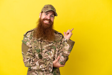 Military Redhead man over isolated on yellow background pointing finger to the side