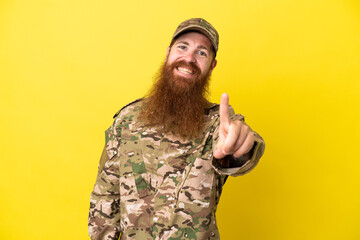 Military Redhead man over isolated on yellow background showing and lifting a finger