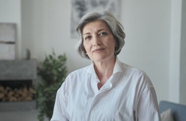 Strong senior mature old businesswoman looks seriously at the camera. Portrait of the Chief Executive in a modern house. Condifent stylish female CEO leader.