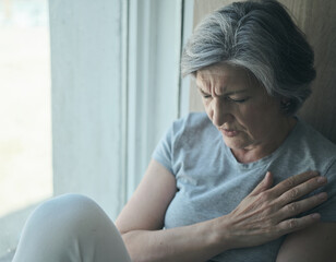 Elderly senior sick disabled, sad woman in pain and suffering sitting by the window in the...