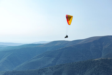 Man on paraglider is flying in the air using a parachute over the mountains behind the blue sky. Extreme sports and freedom