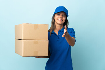 Young delivery woman isolated on blue background shaking hands for closing a good deal