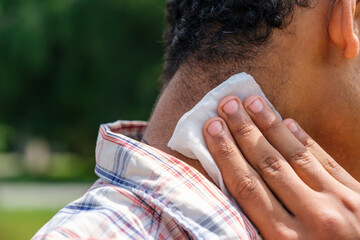 Young Brazilian man disinfecting his neck using a wet wipe close up to prevent infection outdoors...