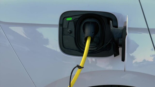 Yellow cable plug charging modern electric vehicle at work or at home