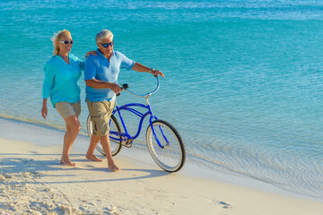 Happy senior couple exercising with bicycles on the beach on a sunny day