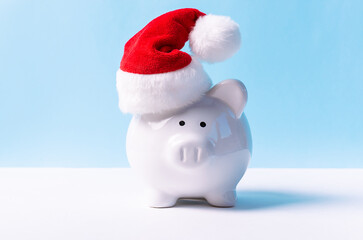 Creative composition with piggy bank in Santa’s hat on white and blue background. Christmas bank promotions and deposits concept. Festive New Year and Christmas shopping.
