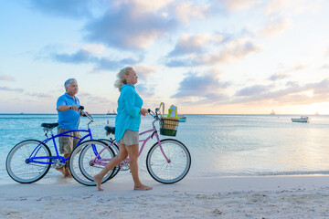 Happy senior couple exercising with bicycles on the beach on a sunny day